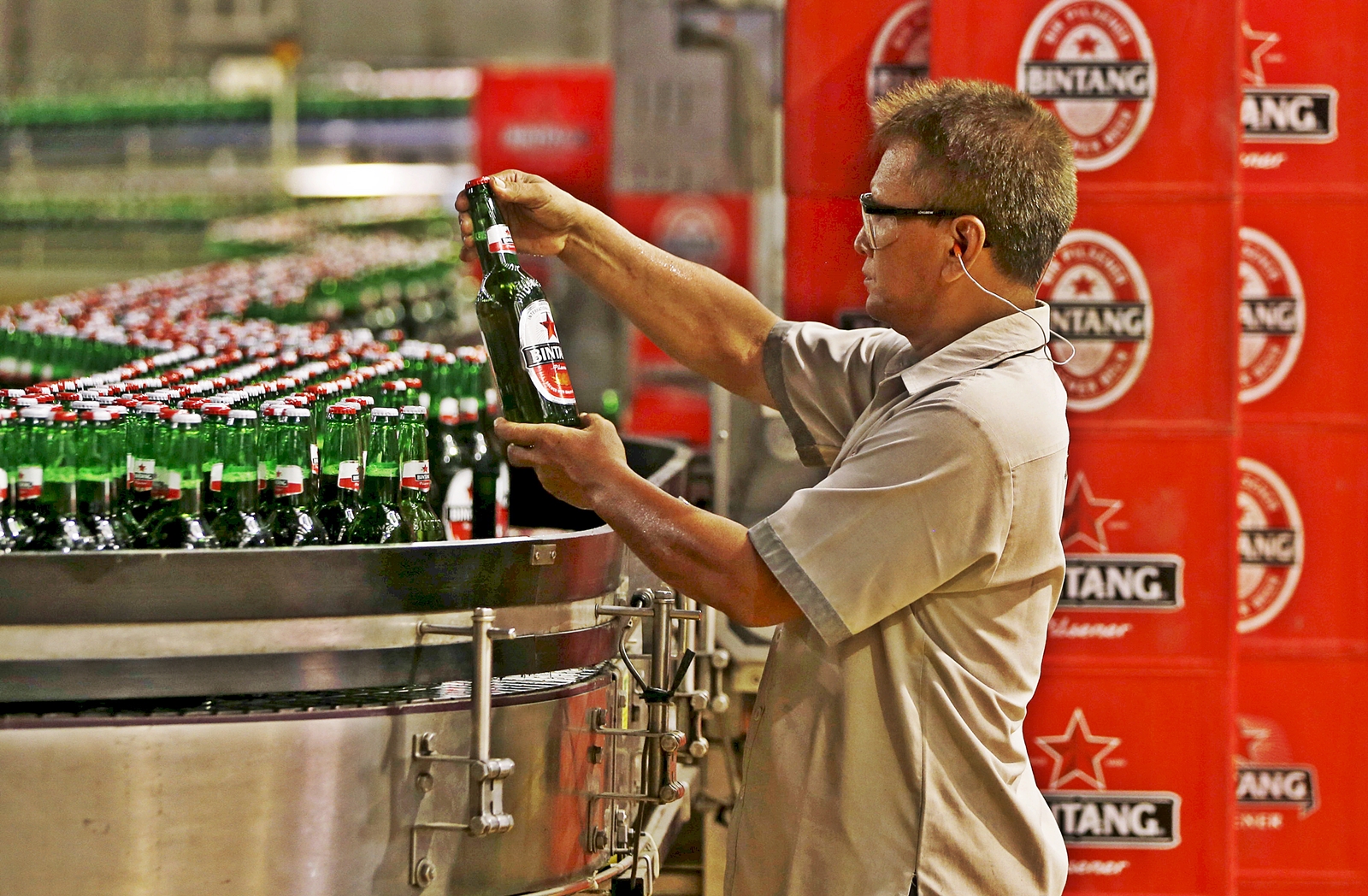 Photo Credit: Pekerja PT Multi Bintang Indonesia Tbk. memegang sebotol bir Bintang untuk memeriksa kualitas di sebuah pabrik bir di Jakarta 17 April 2015. REUTERS
